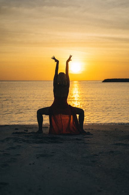 Silhouettes of two people in a yoga balance pose during a colorful sunset.